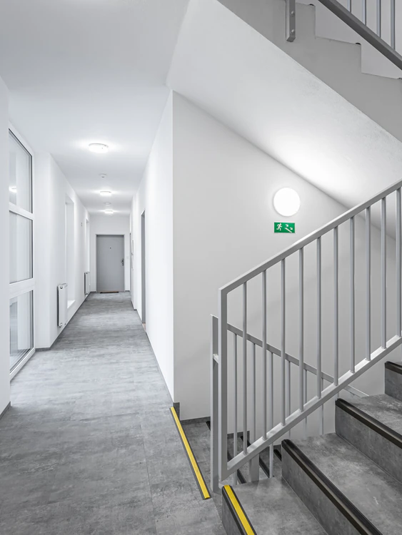 Emergency bulkhead luminaire and exit sign in a building stairwell