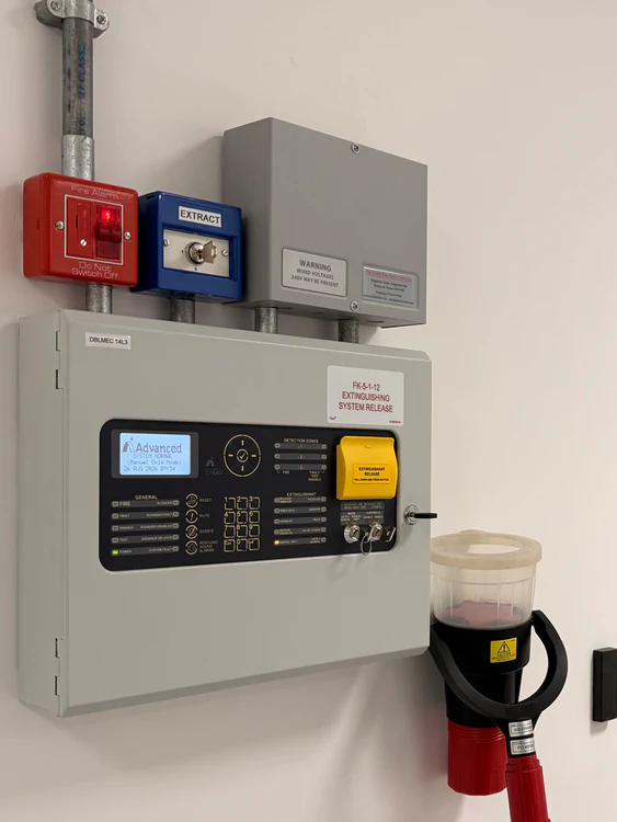 Advanced extinguishing system release panel labelled FK-5-1-12 alongside a fire alarm call point and manual release